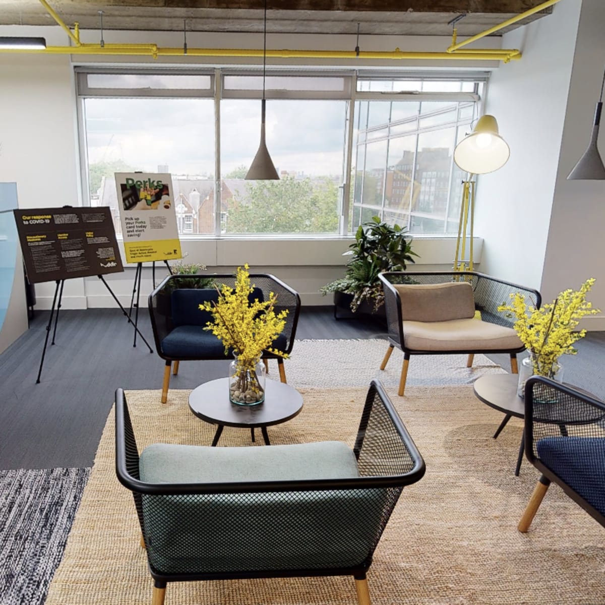 A modern office lounge area with potted plants, seating arrangements, and a large colorful partition.