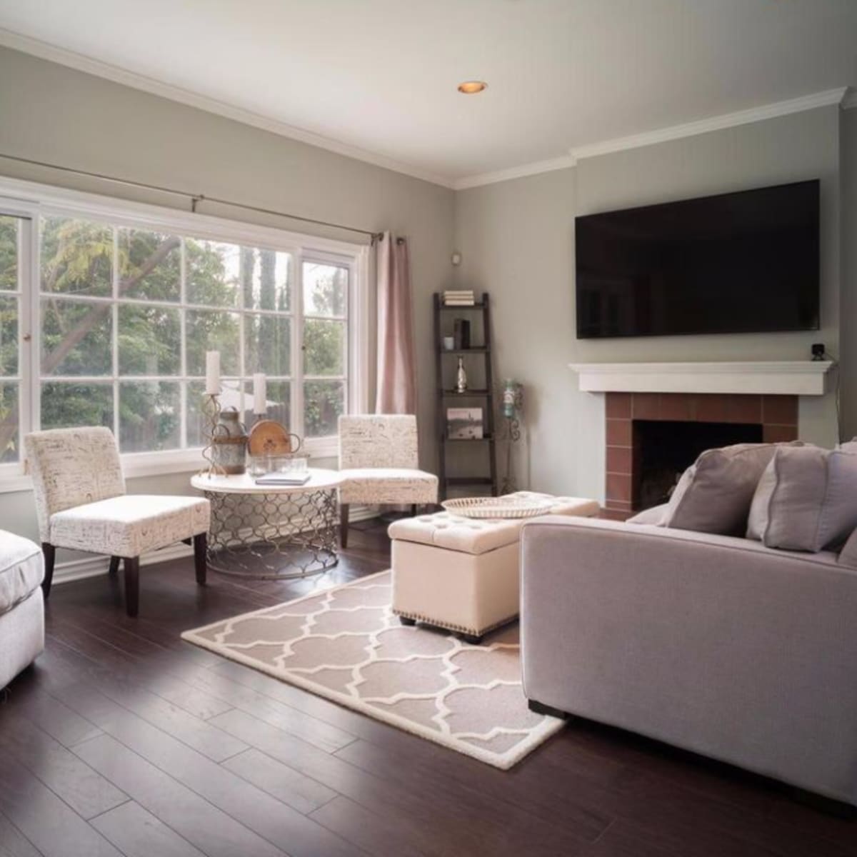 The living room features a large window, two armchairs, a circular coffee table, and a sectional sofa arranged around a fireplace.