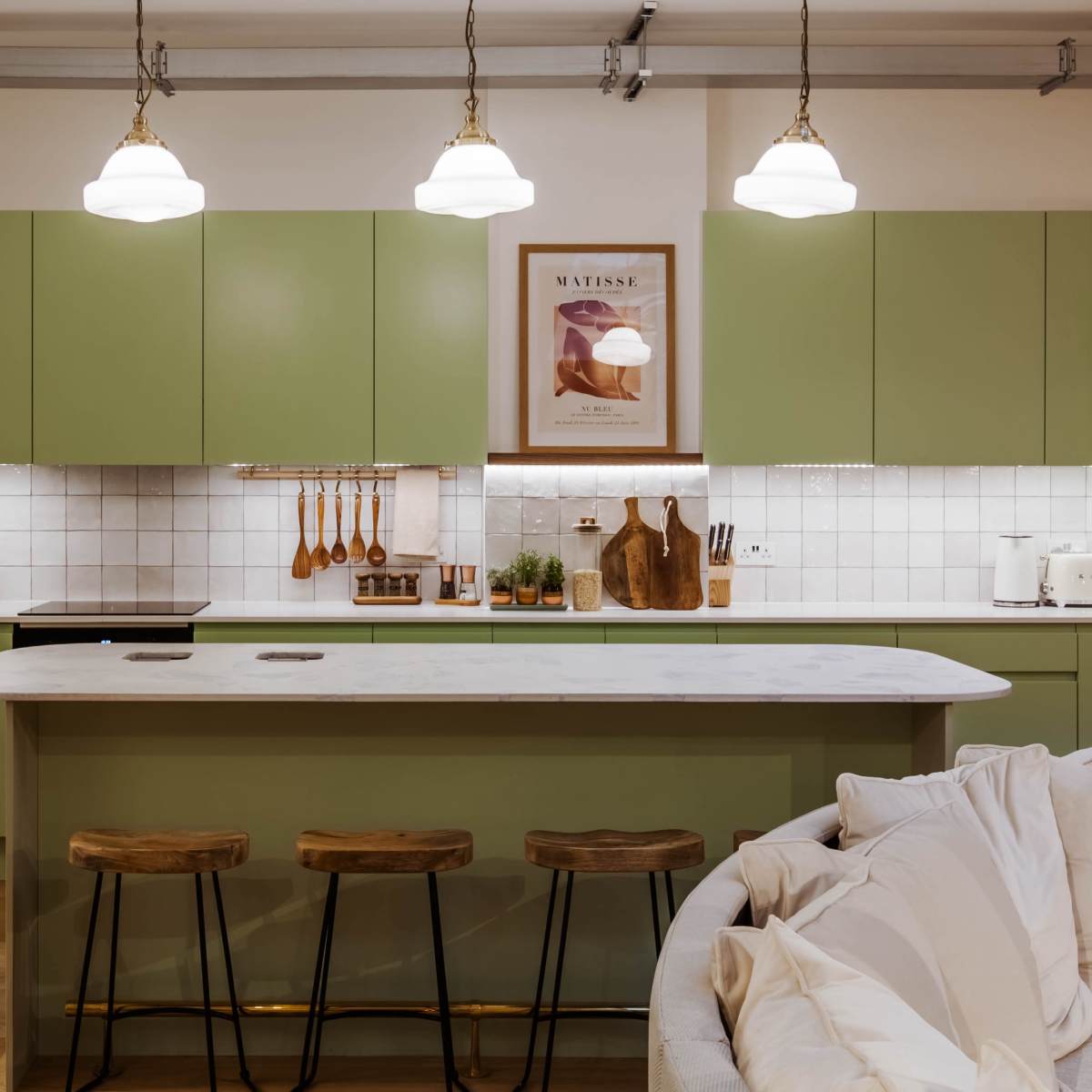 A modern kitchen with green cabinets, a white marble countertop, and three wooden stools at the island.