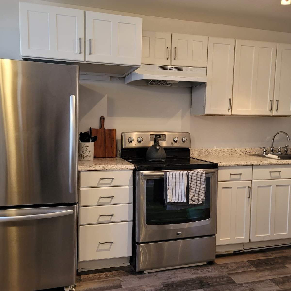 A modern kitchen with white cabinets, a stainless steel refrigerator, and an oven, featuring a granite countertop and a sink.