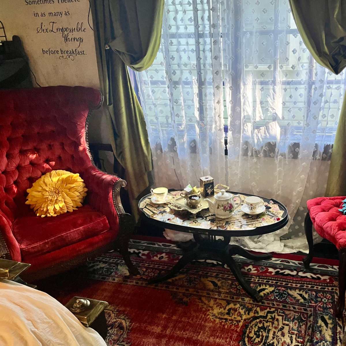 The scene depicts a quaint seating area with two red velvet chairs, a decorative coffee table covered in tea set items, and a window adorned with lace curtains.