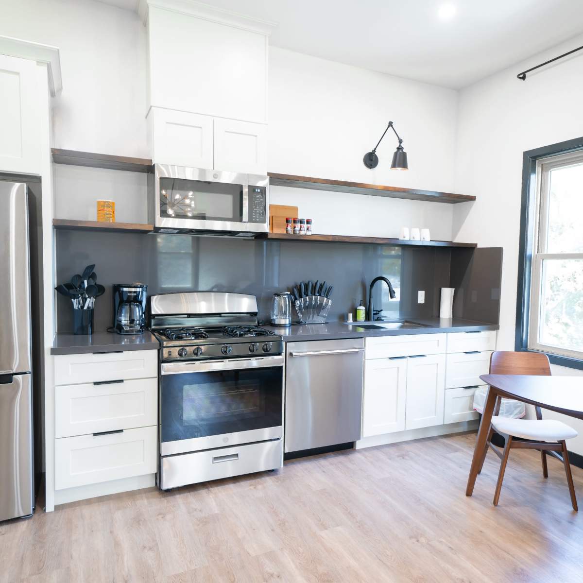 A modern kitchen with stainless steel appliances, white cabinetry, and a circular wooden dining table with two chairs.