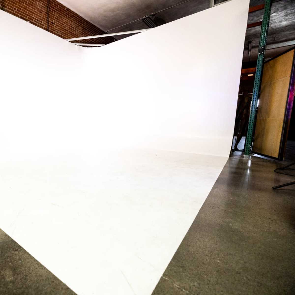 A spacious studio features a large, white backdrop meeting the floor at a sharp angle.