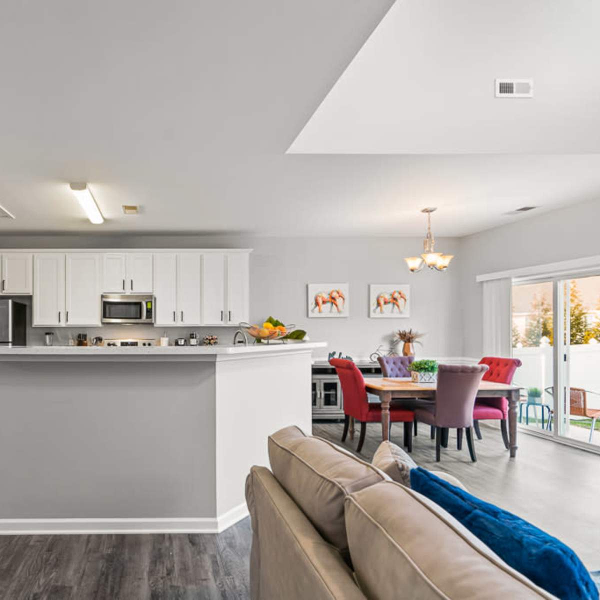 A modern kitchen with white cabinets and stainless steel appliances opens up to a dining area featuring a colorful table and chairs.