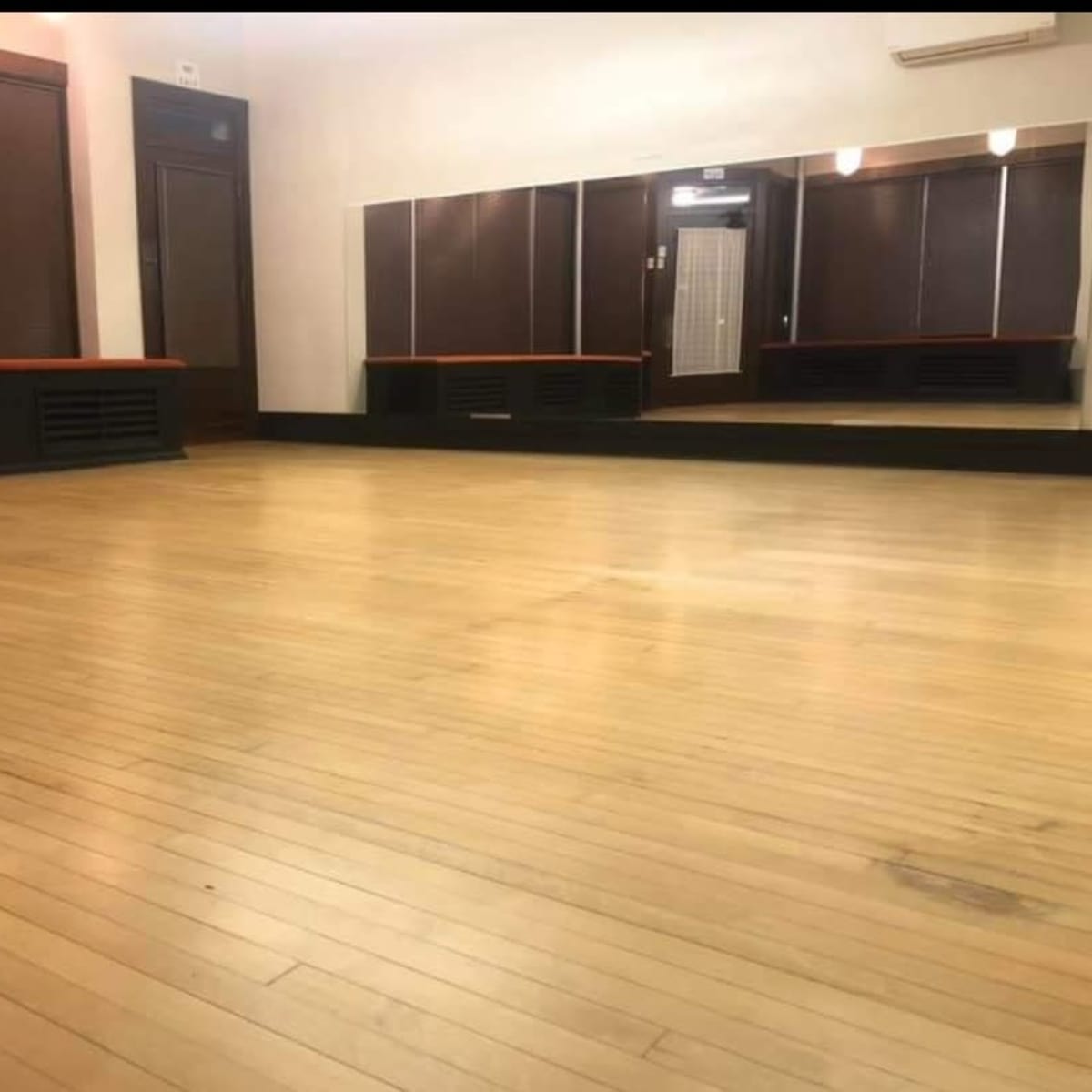 A spacious room with wooden floors, large mirrors on one wall, and dark blinds covering the windows.