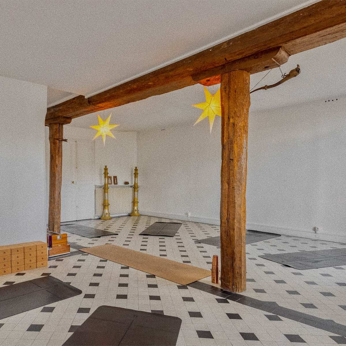 A spacious room with a patterned tiled floor, wooden beams, and a few boxes stacked on one side.