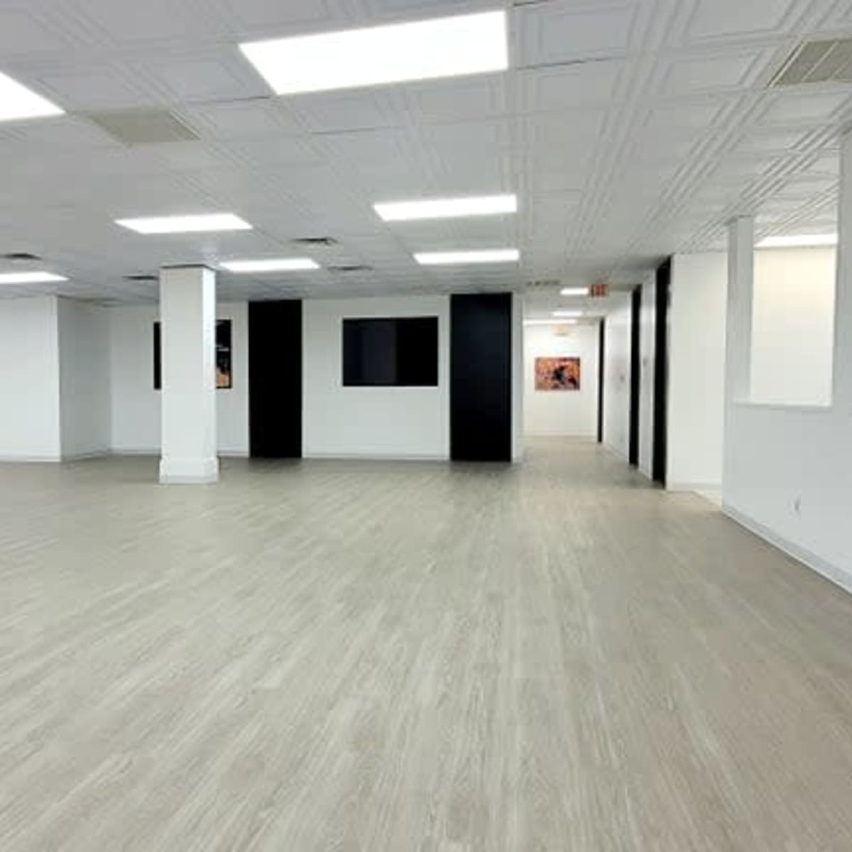 A spacious, empty room with light-colored flooring and white walls, featuring a few partitions and large windows.