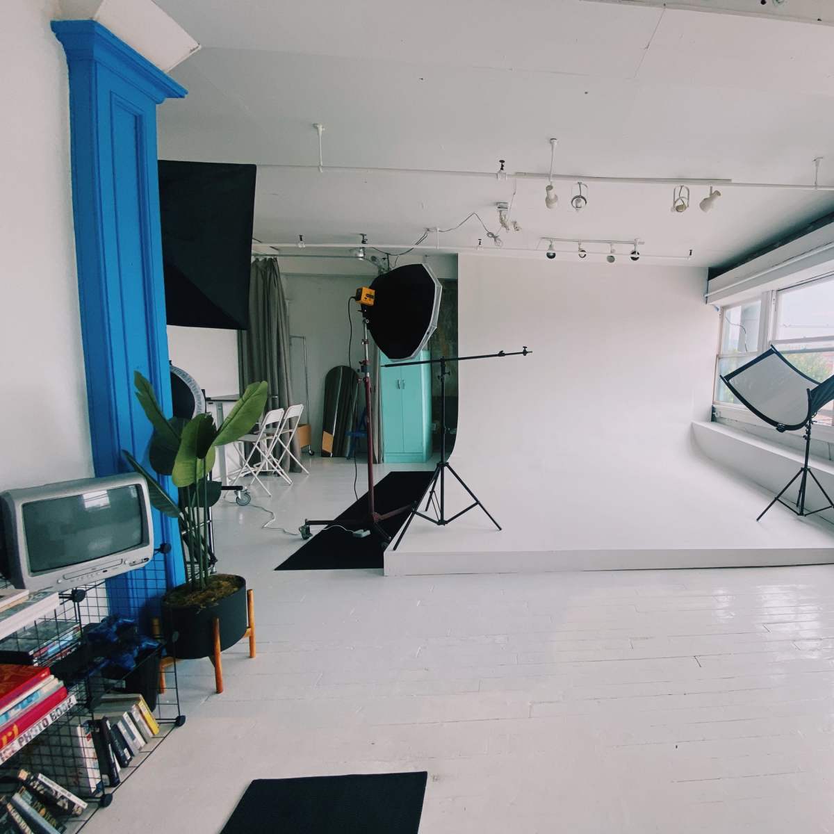 A photography studio with a white backdrop, lighting equipment, a vintage television, and various shelves filled with items.