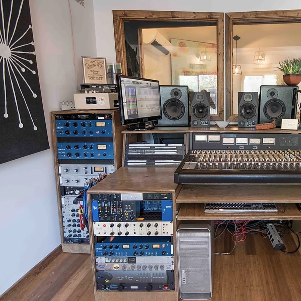 A recording studio setup featuring a large mixing console, audio equipment racks, speakers, a computer monitor, and a wood-paneled interior.