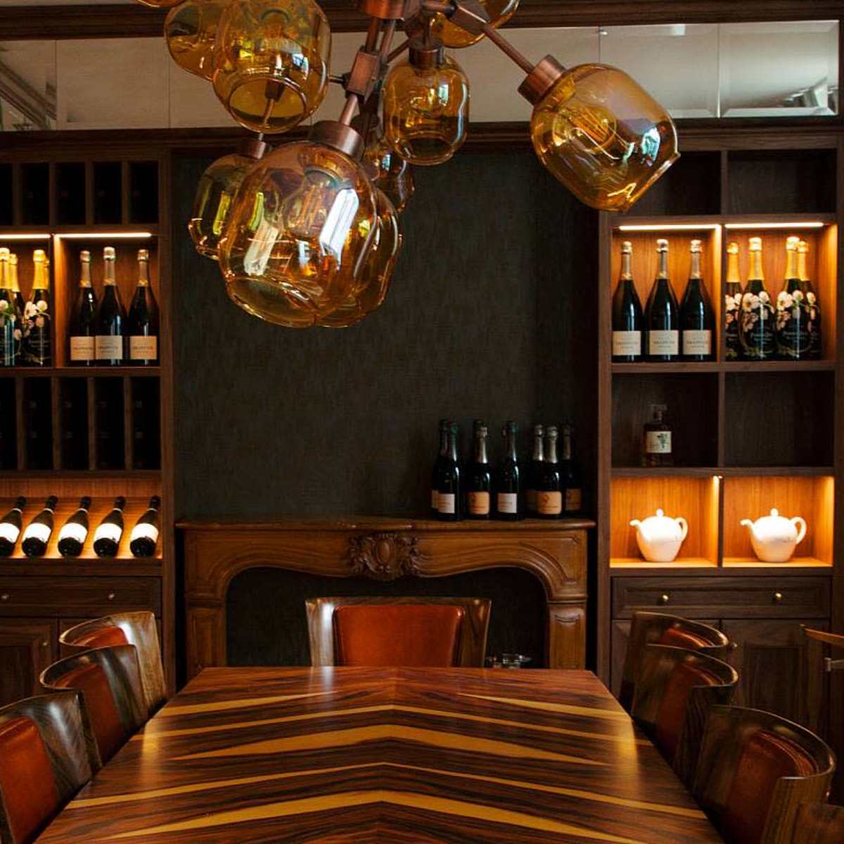 A private dining room featuring a wooden table surrounded by leather chairs, with shelves of champagne bottles and decorative lighting.