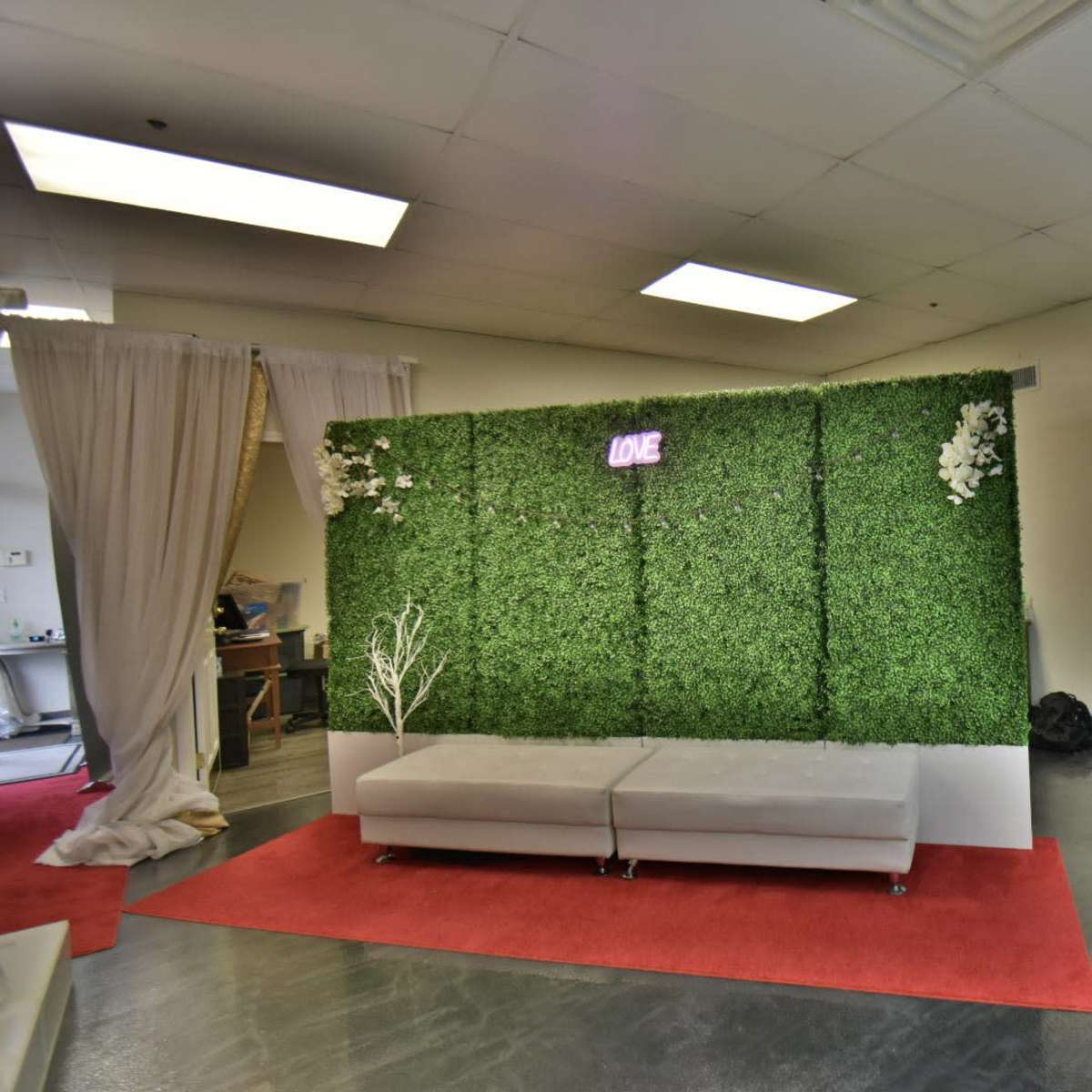 A small interior space featuring a green moss wall with the word "LOVE" illuminated, a gray sofa, and a red carpet.
