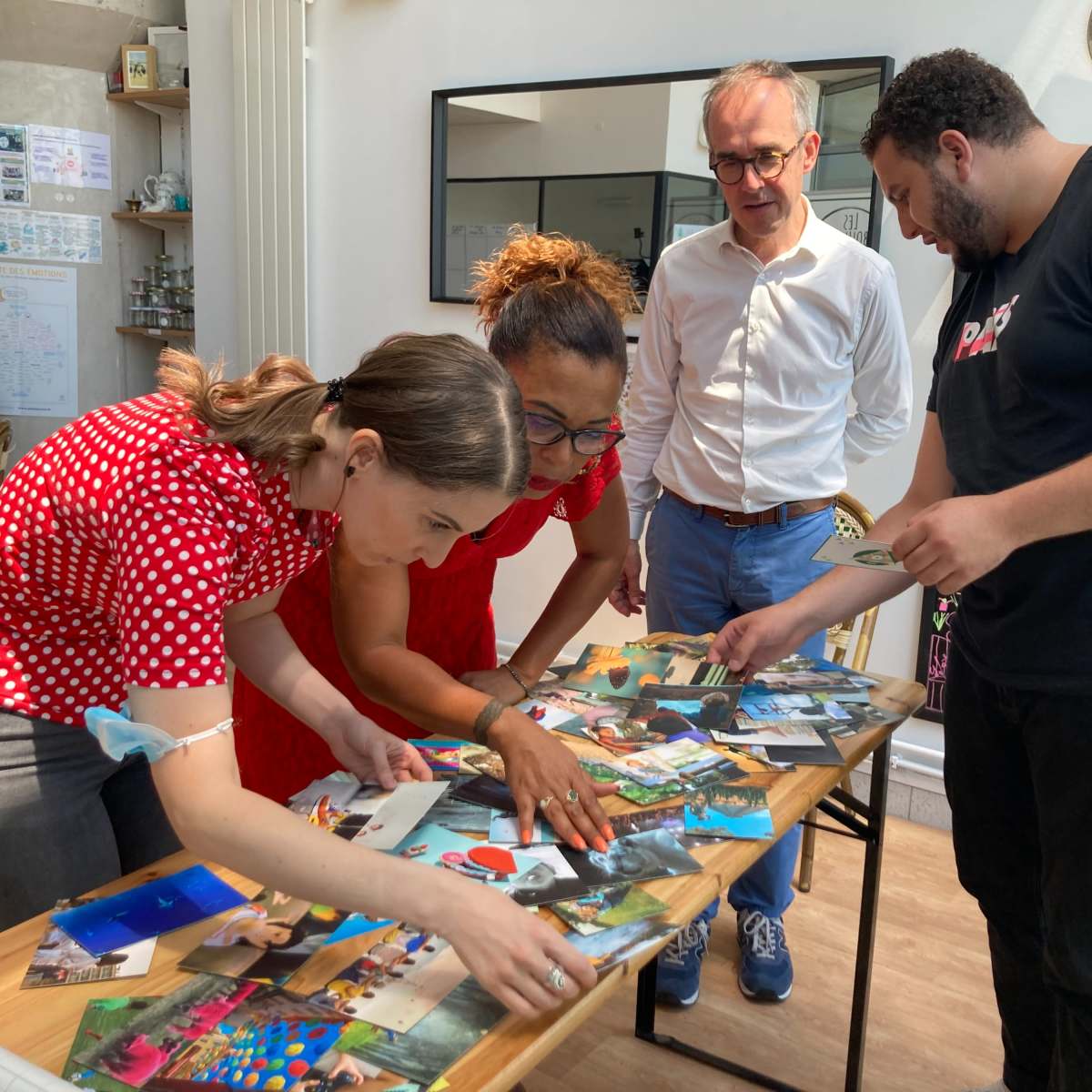 A group of four people is examining a collection of photographs on a table in a bright, decorated room.