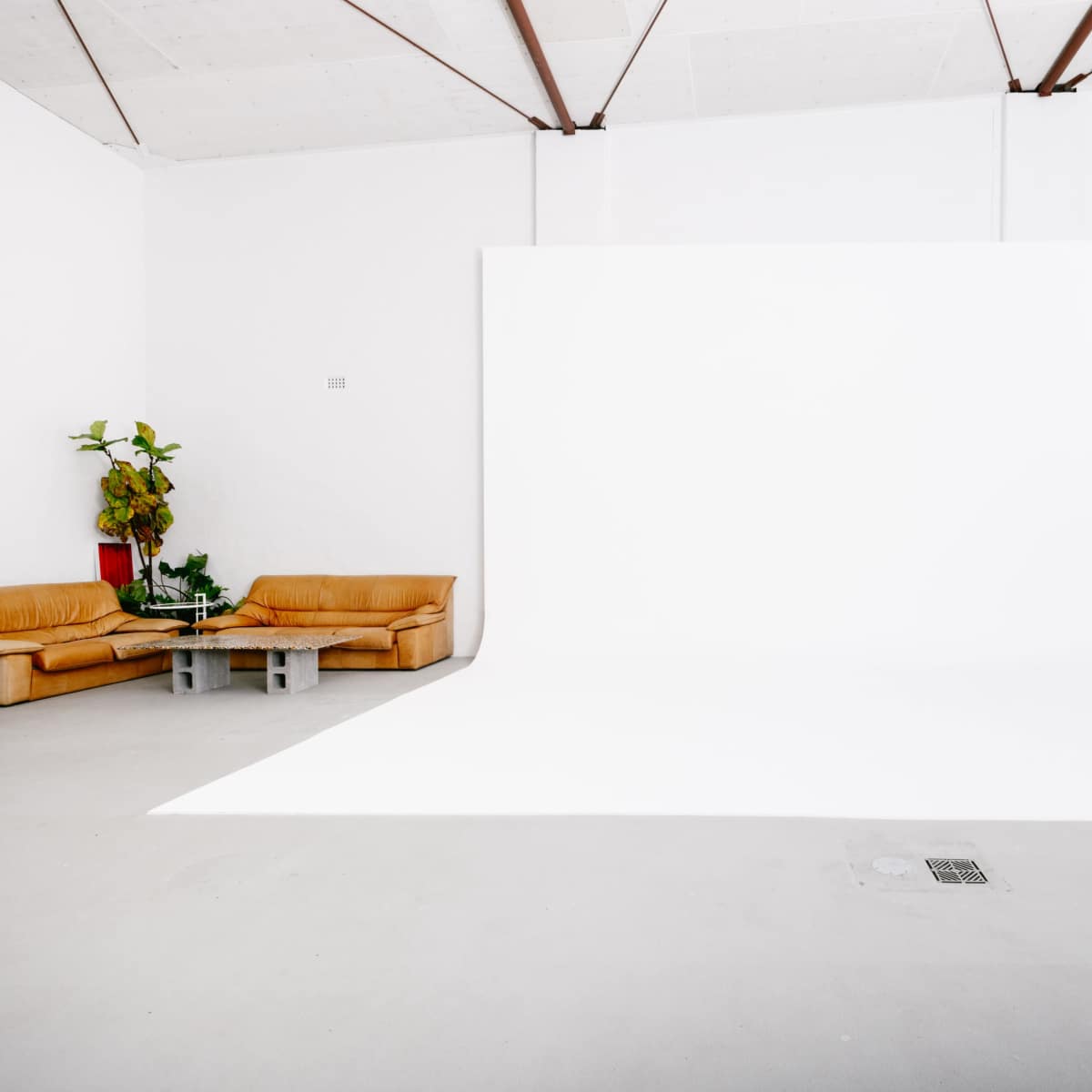 A spacious, minimalist studio with a white backdrop, two tan couches, and a small table surrounded by metal chairs.