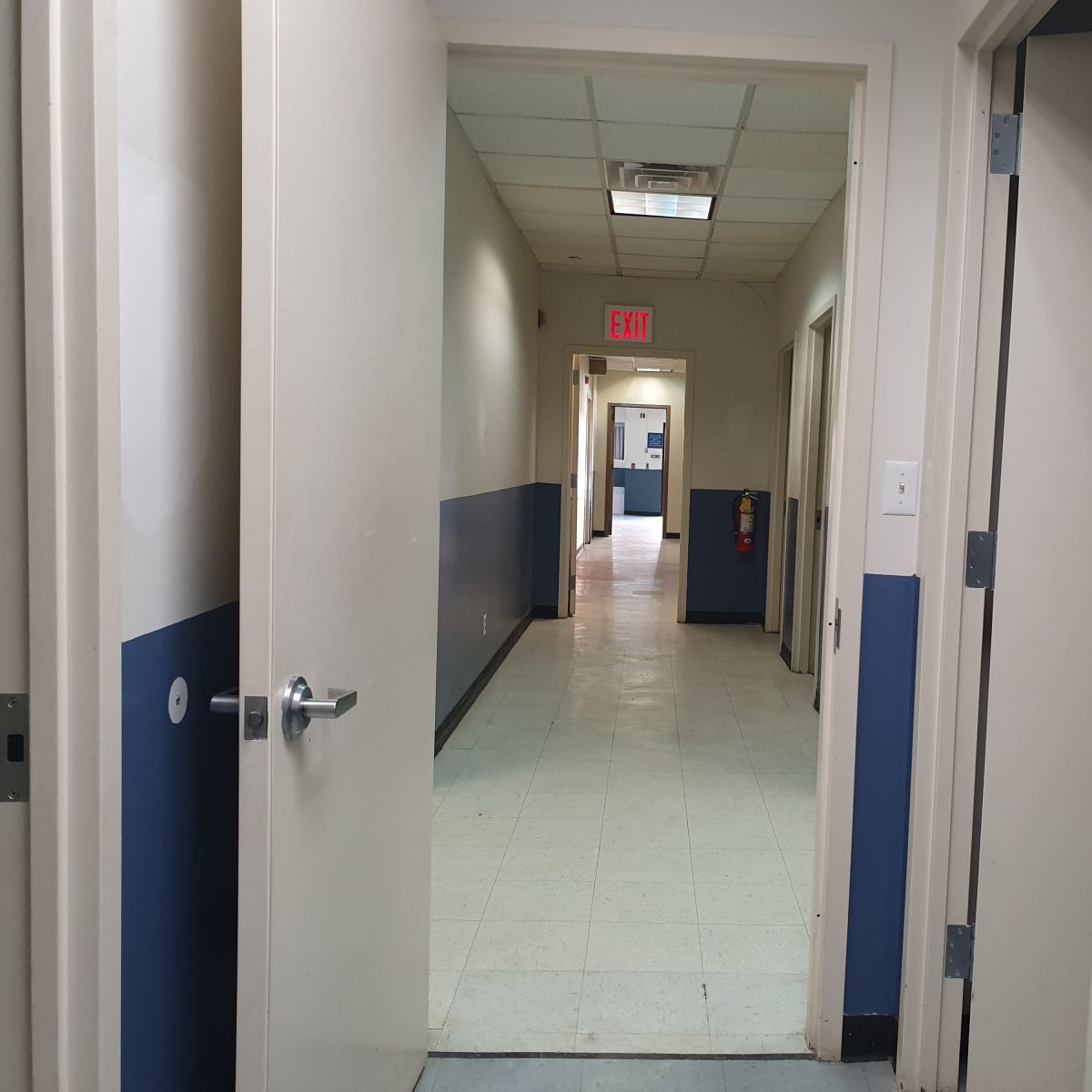 A long hallway with doors on either side and exit signage at the far end.