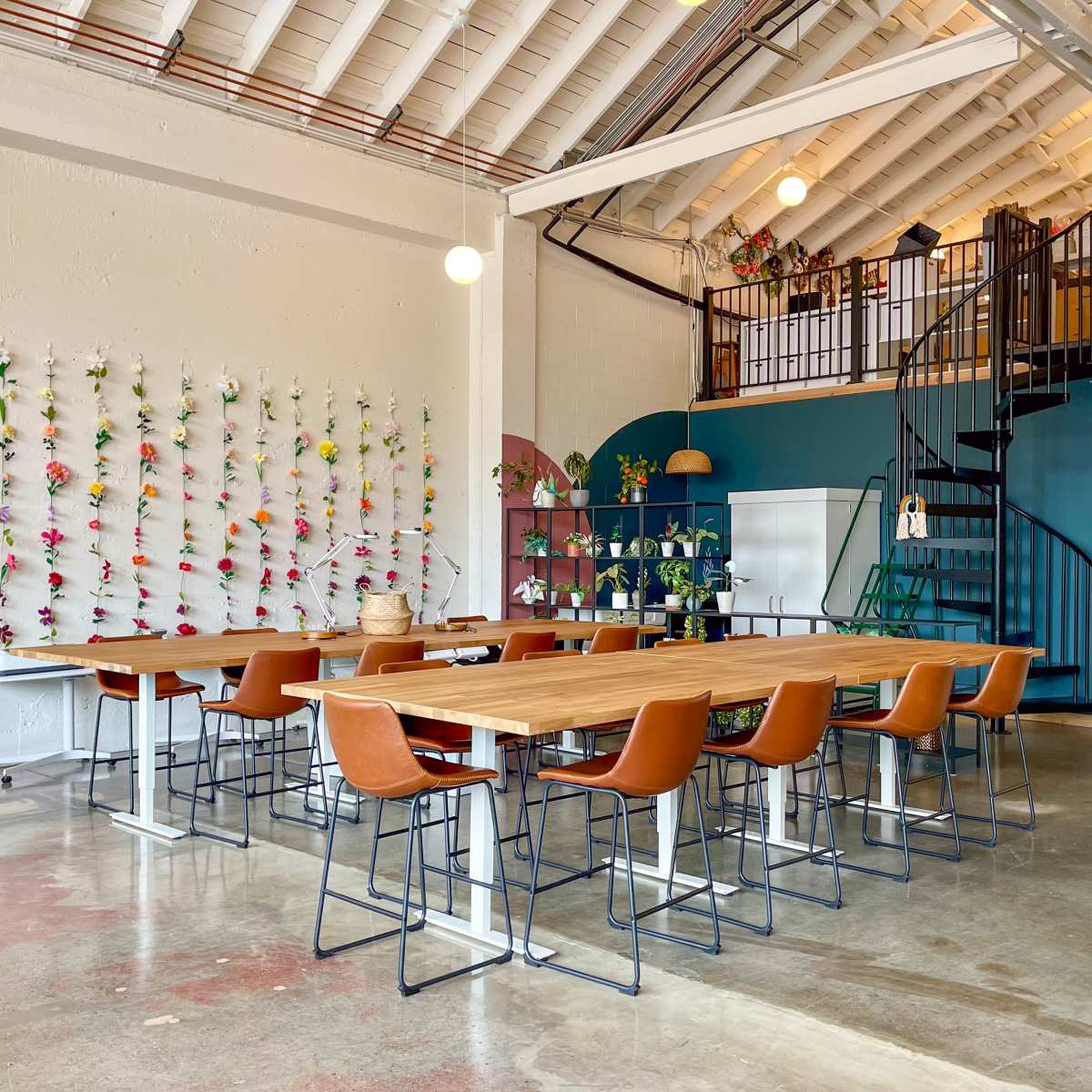 A spacious meeting room with a long wooden table surrounded by high-backed chairs, located beneath a loft area with a spiral staircase and decorated walls.