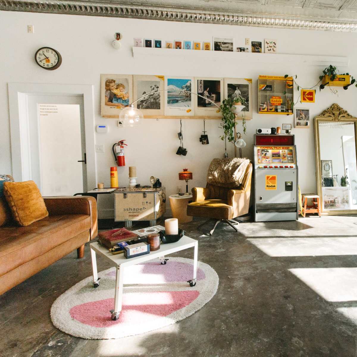 A cozy indoor space with a brown sofa, a vintage armchair, art on the walls, and various plants arranged throughout.