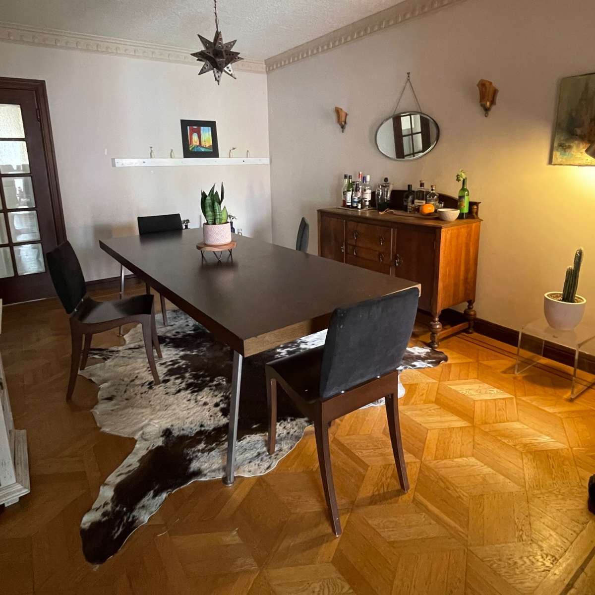 A spacious dining area features a long table, black chairs, a wooden sideboard, and decorative wall accents.