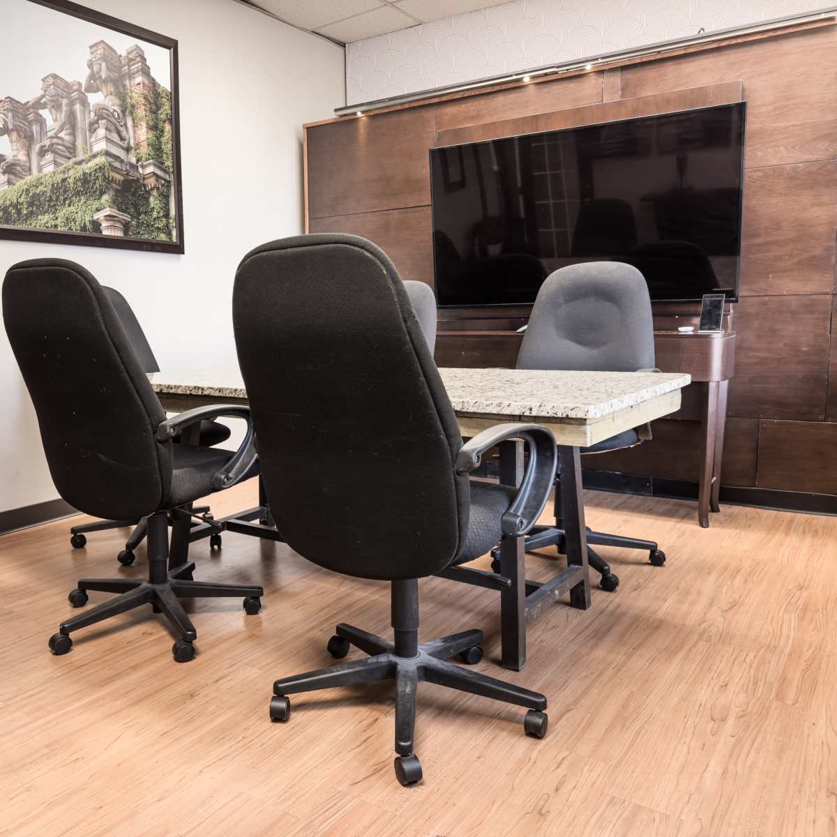 A conference room with a large table surrounded by four rolling chairs and a television mounted on the wall.
