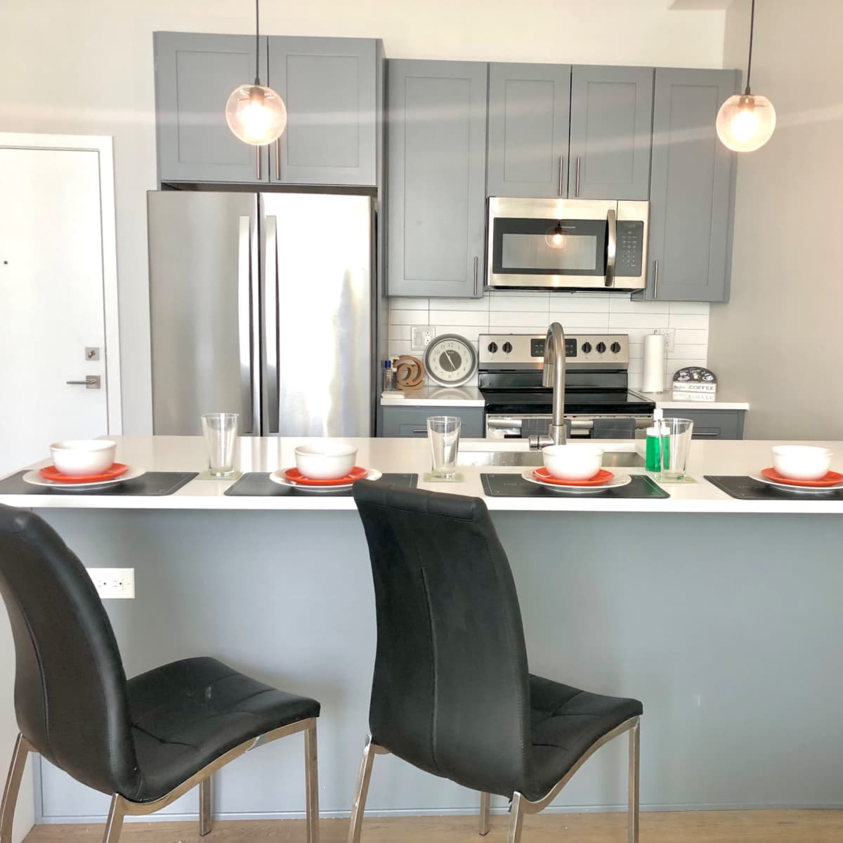 A modern kitchen features gray cabinets, stainless steel appliances, and a countertop with four place settings at a bar.
