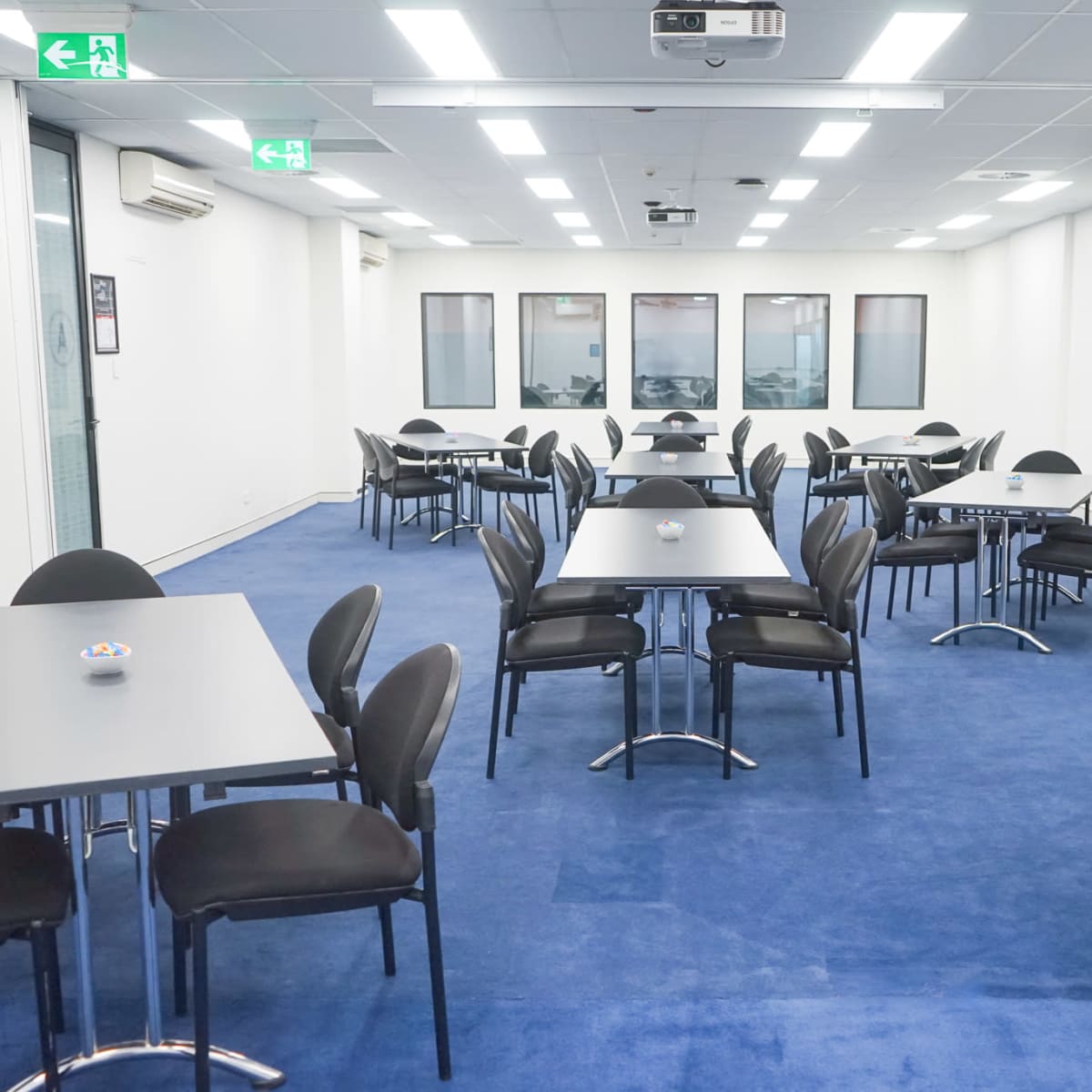 A modern conference room with multiple black chairs and tables arranged on blue carpet.