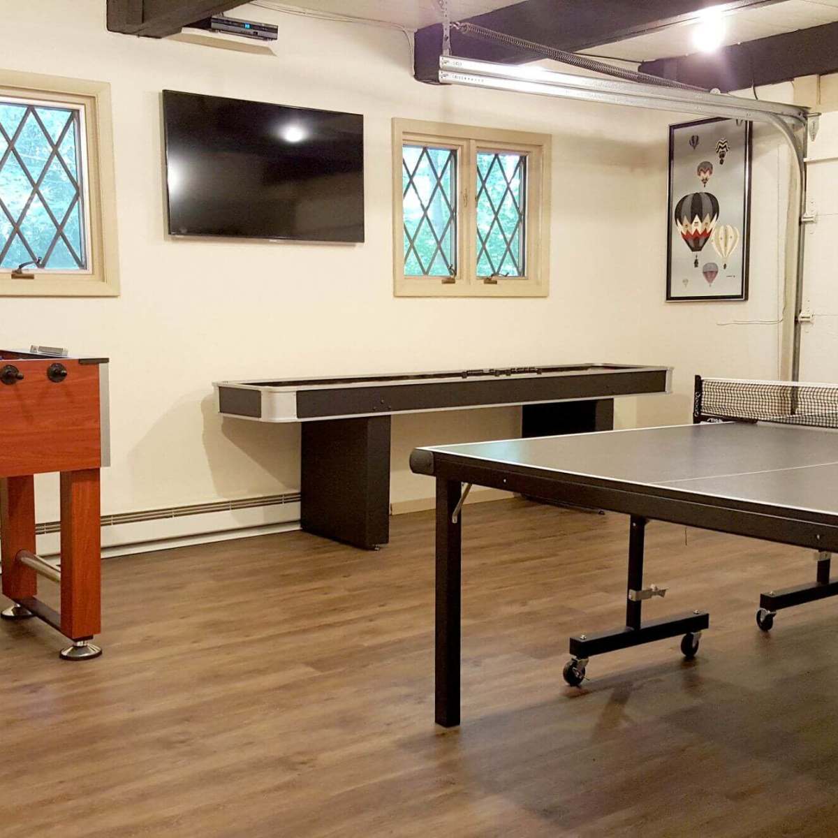 A recreational room with a foosball table, a ping pong table, and a wall-mounted television.