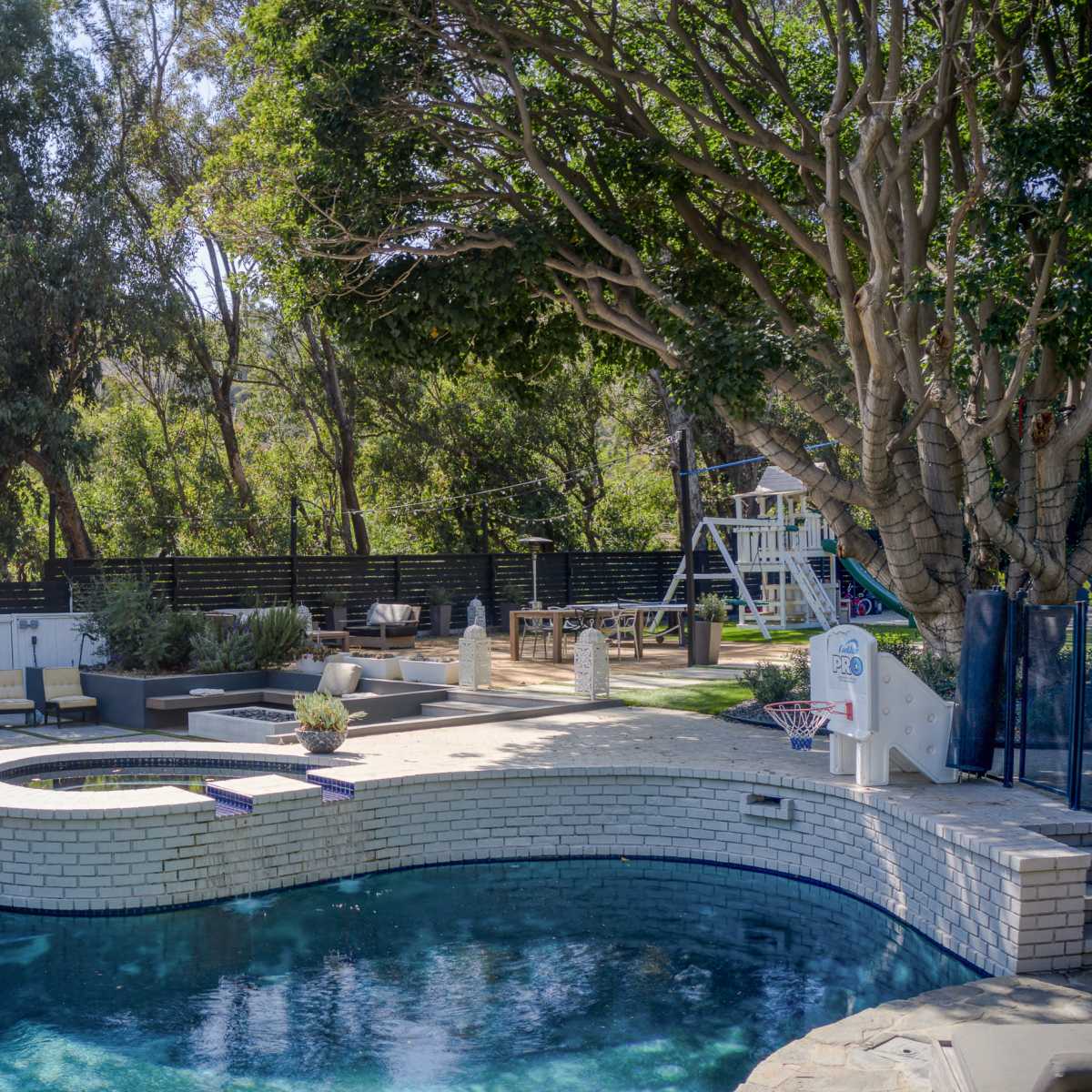 A backyard with a swimming pool, surrounded by trees, lounge chairs, and a small outdoor dining area.
