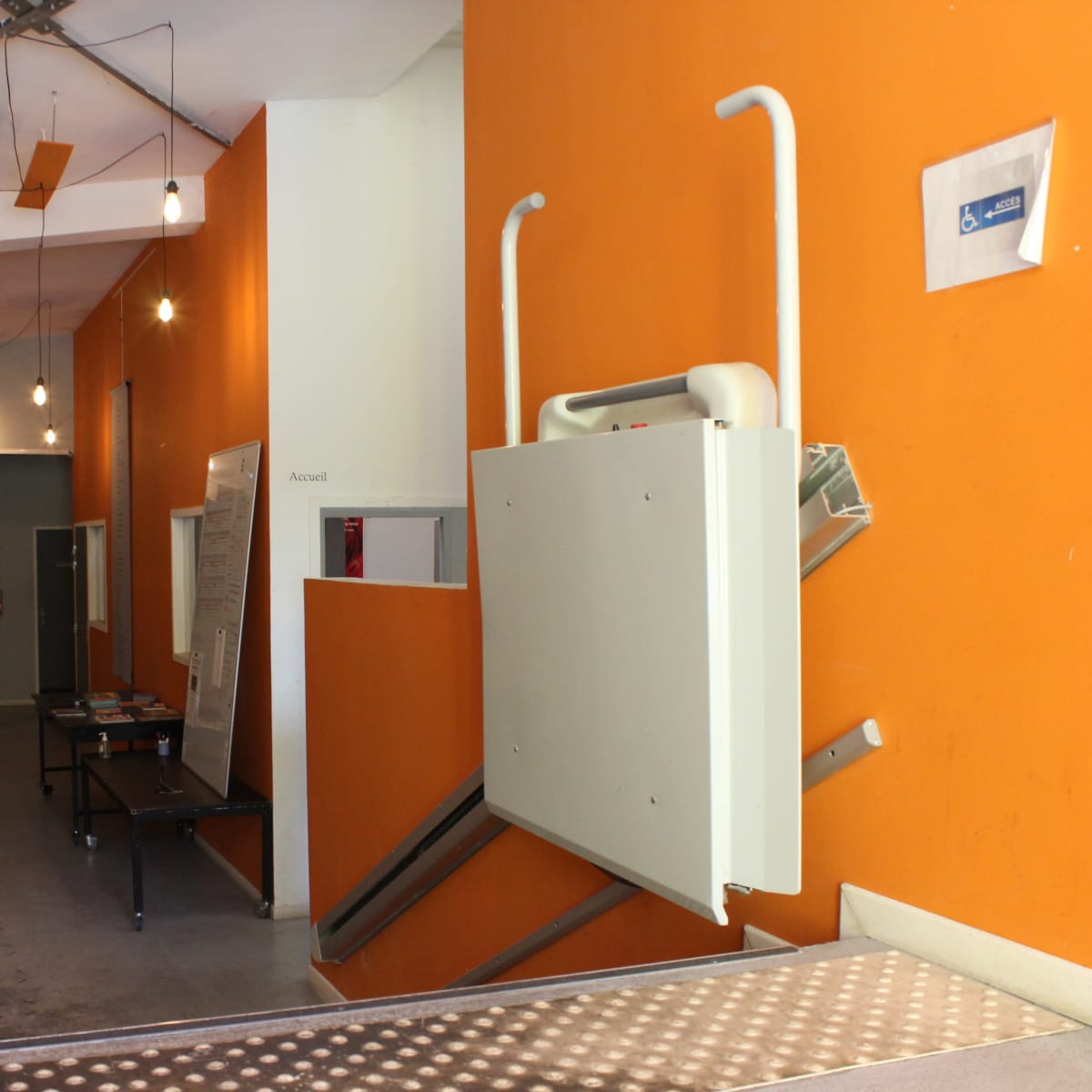 A hallway with an orange wall, a ramp for accessibility, and a table against the opposite wall.