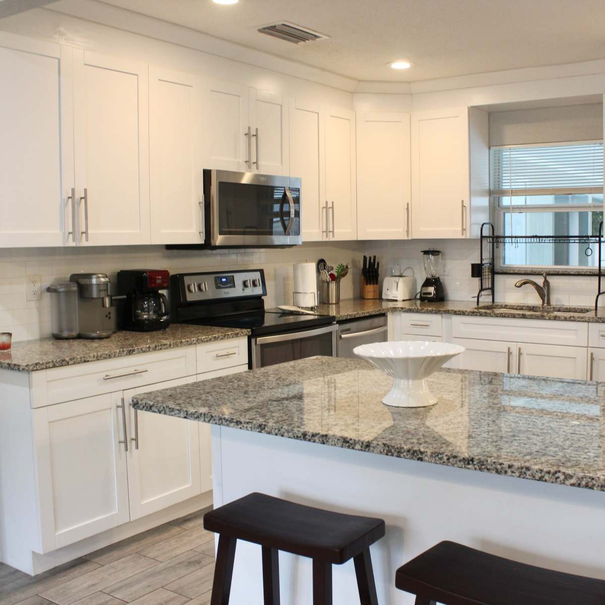 A modern kitchen with white cabinets, stainless steel appliances, a granite countertop, and an island with two wooden stools.