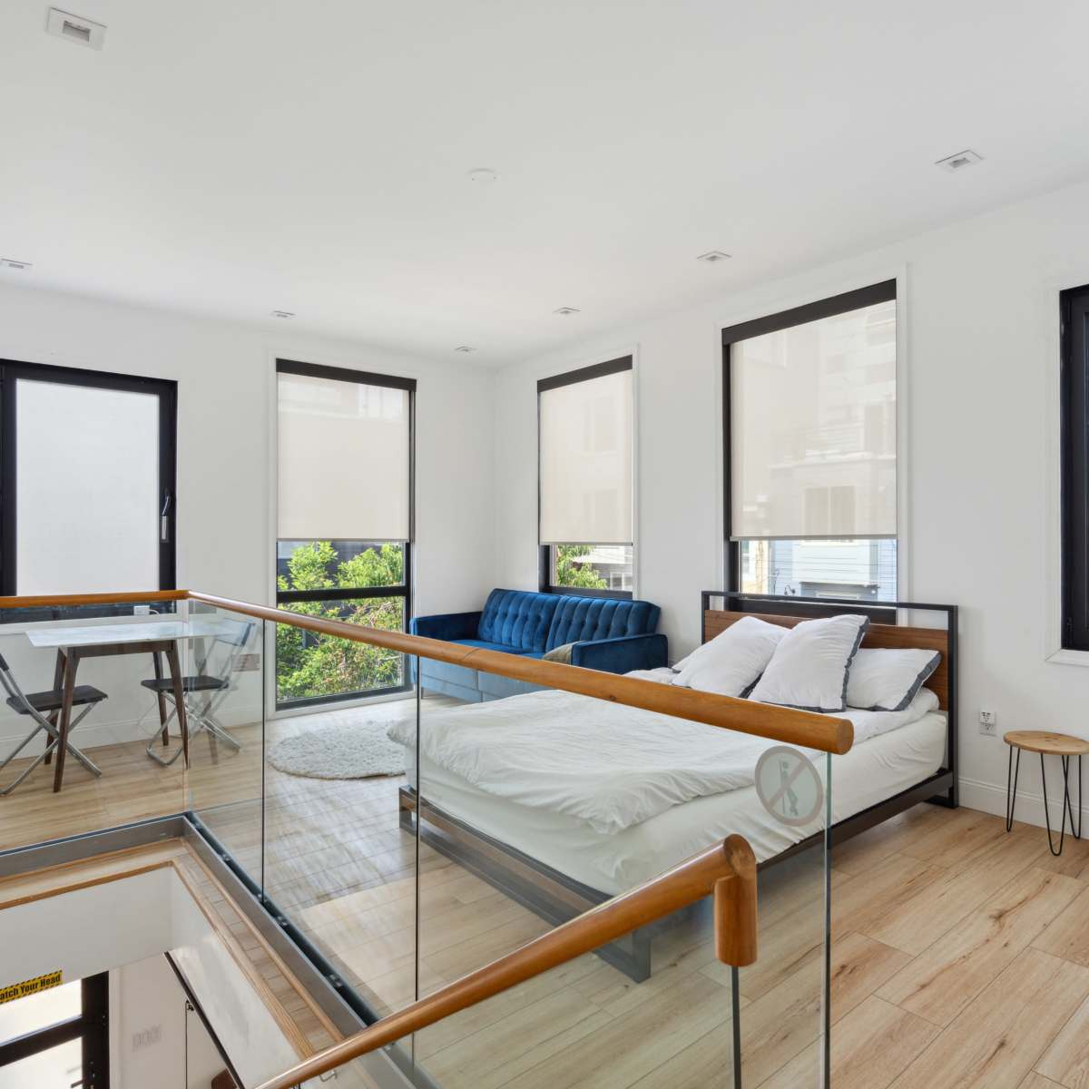 A modern, open-concept bedroom and seating area with large windows and a wooden floor.