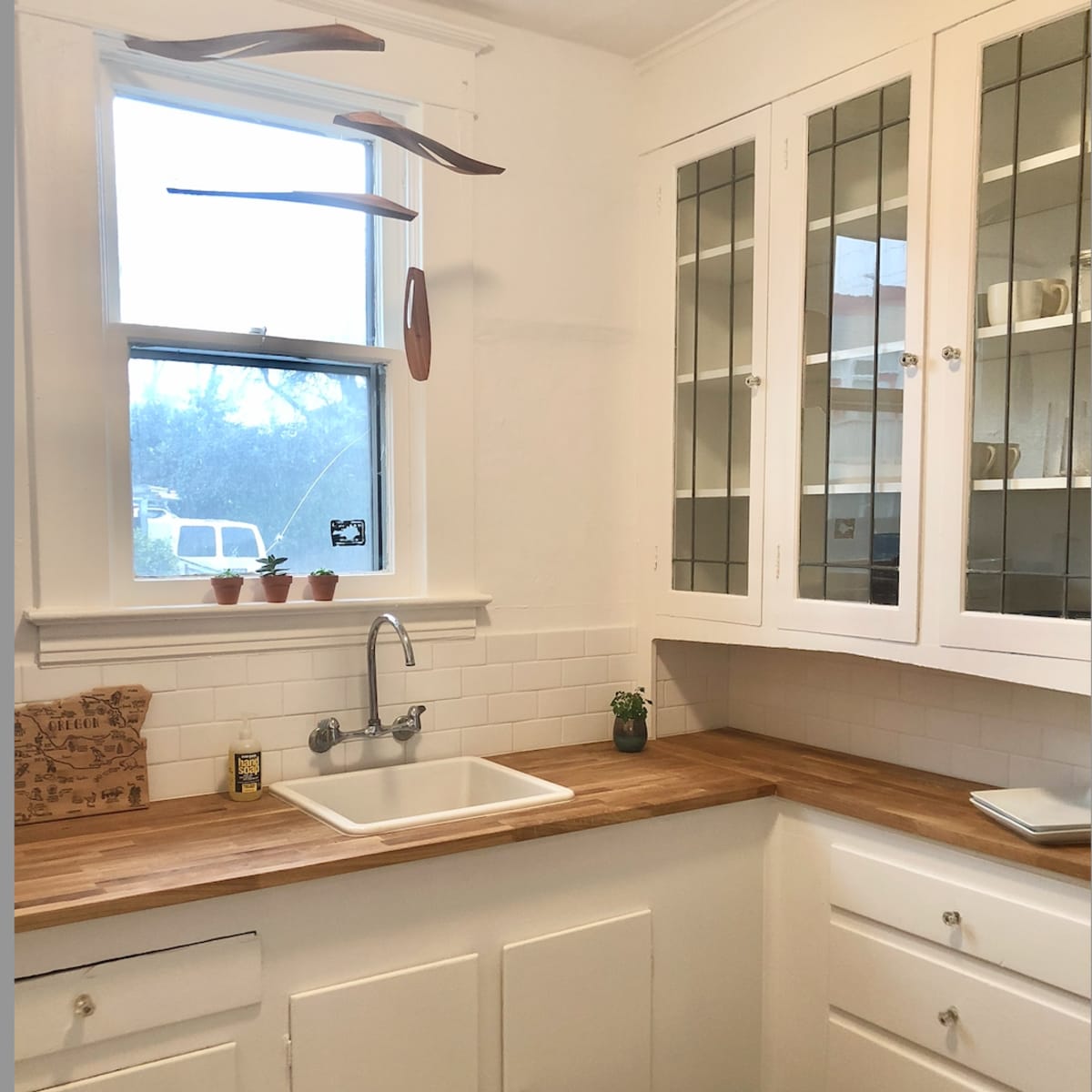 A modern kitchen with white cabinets, a wooden countertop, a farmhouse sink, and a window letting in natural light.