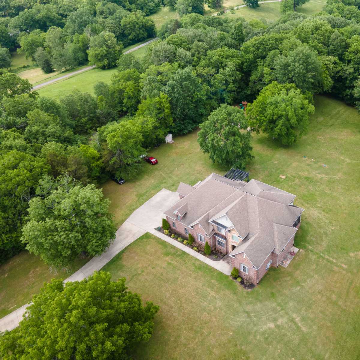 An aerial view shows a large brick house surrounded by a green expanse of trees and grass.