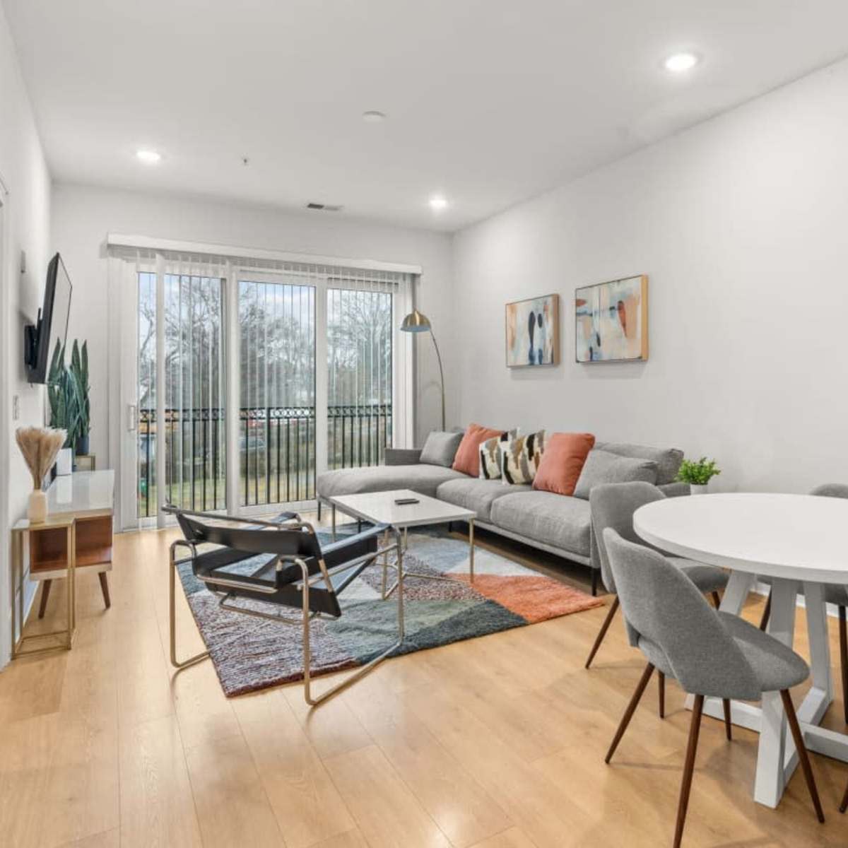 A modern living room features a gray sofa, a round dining table with chairs, and large sliding glass doors leading to a patio.