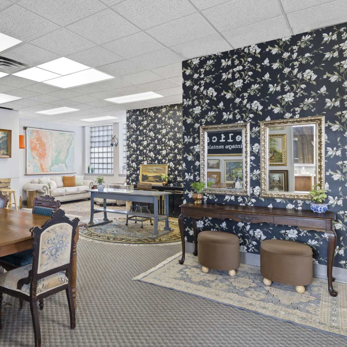 A spacious office area featuring a dining table with chairs, a seating area with a couch, and decorative floral wallpaper.
