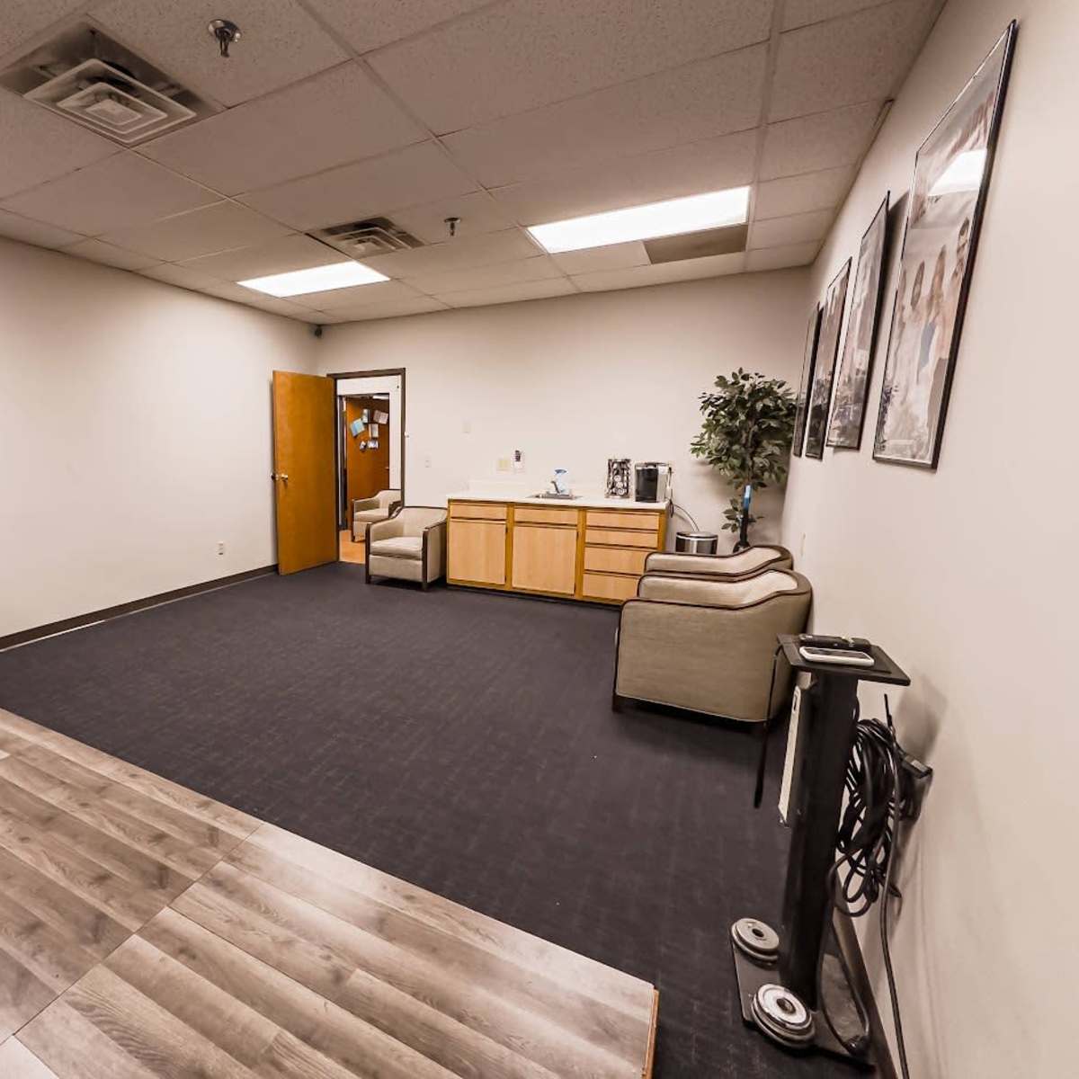 A sparsely furnished office space with a small couch, a stool, and wooden flooring.