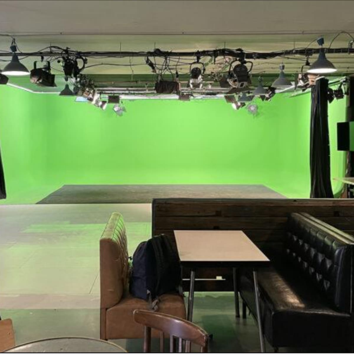 A studio space with a green screen backdrop, surrounded by various seating arrangements and lighting fixtures.