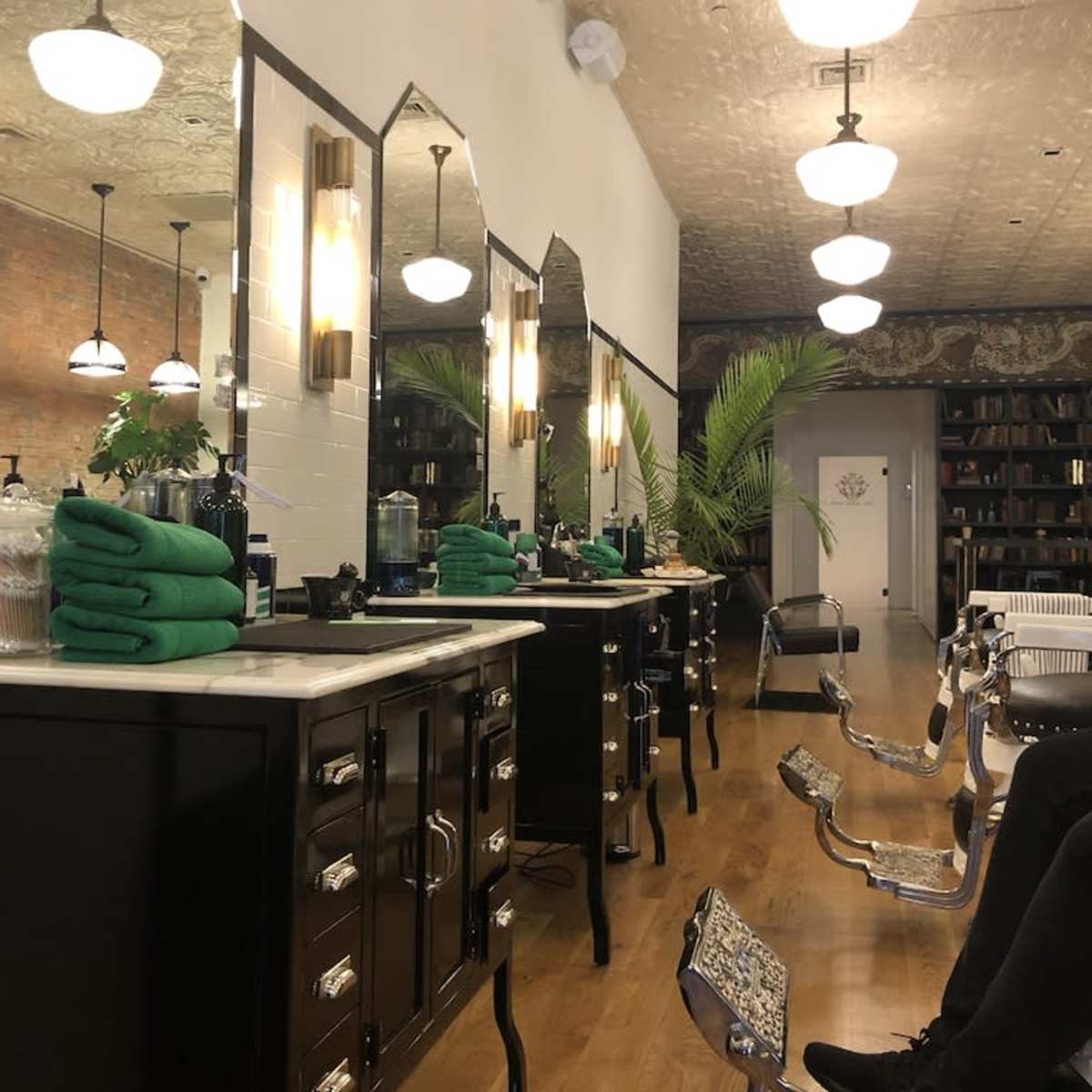 A modern salon interior with black cabinetry, mirrors, and barber chairs, complemented by green towels and potted plants.
