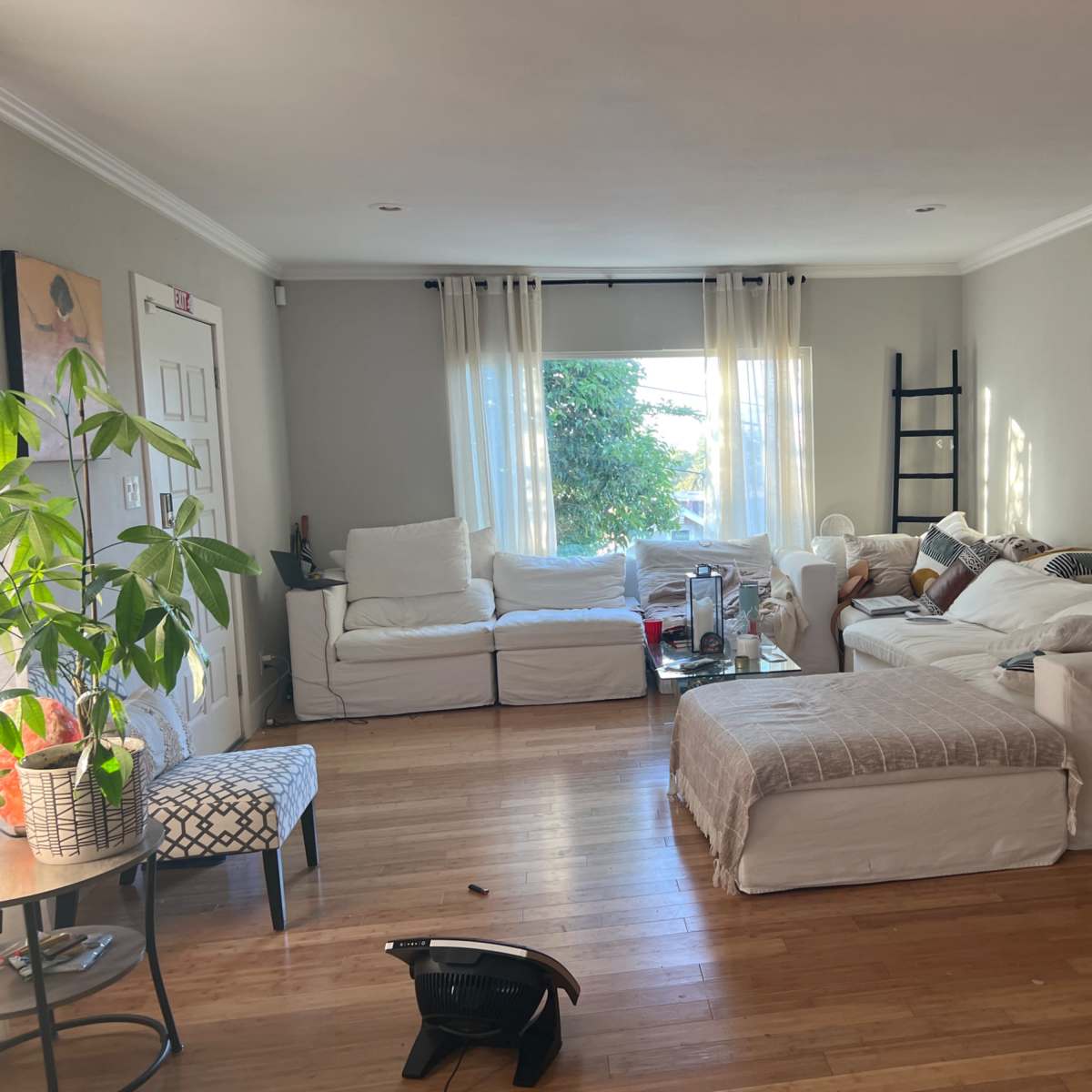 A living room with two white sofas, a coffee table, a decorative chair, and large windows letting in natural light.
