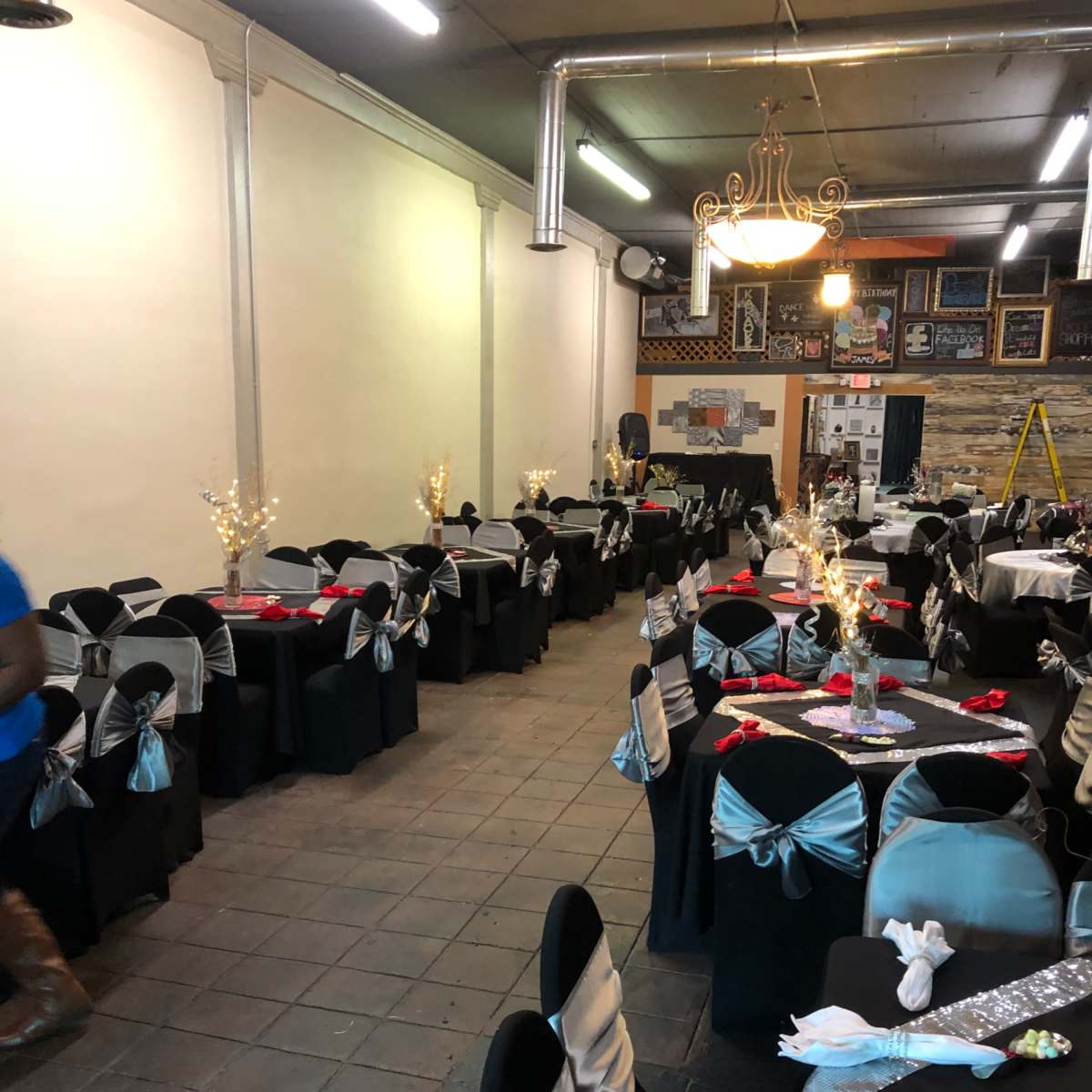 A banquet hall arranged with several tables covered in black tablecloths and decorated with silver and red accents.