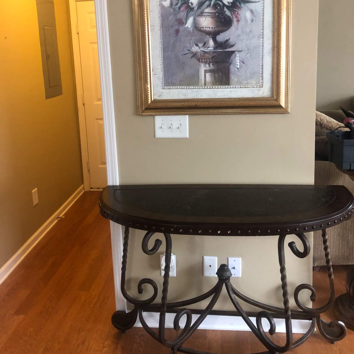 A console table against a wall with a framed floral painting above it, leading to a hallway on the left.