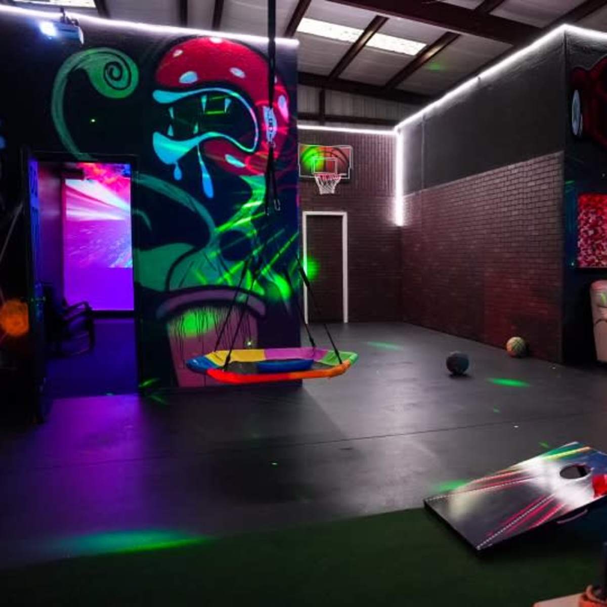 A vibrant indoor recreational space featuring colorful murals, a couch, a hanging swing, and various playful decorations illuminated by glowing lights.