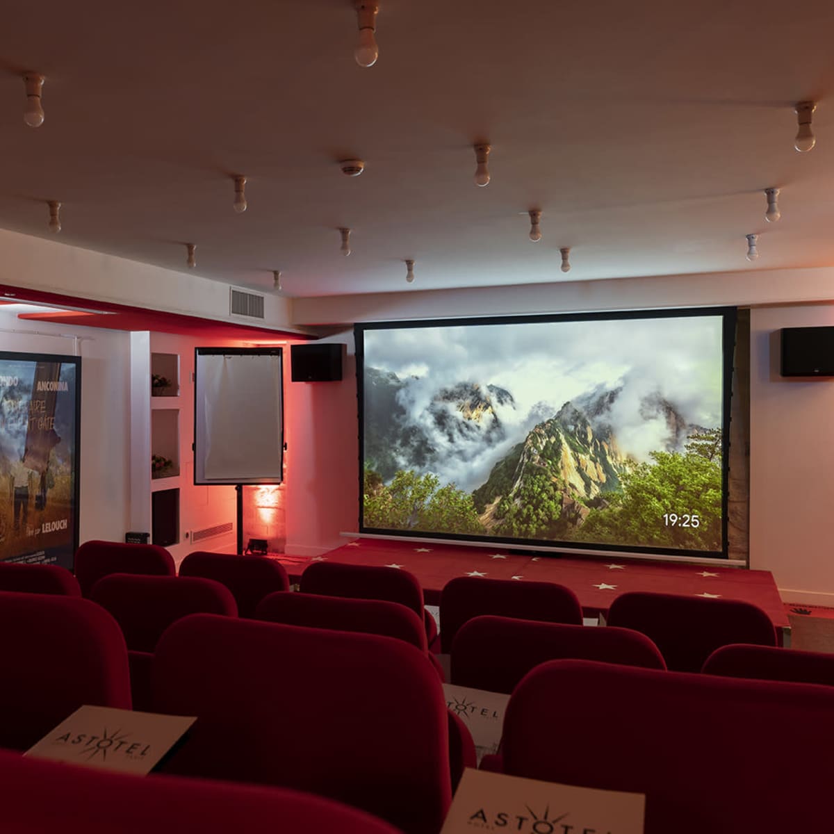 A small theater with red seating and a large screen displaying a mountain scene.