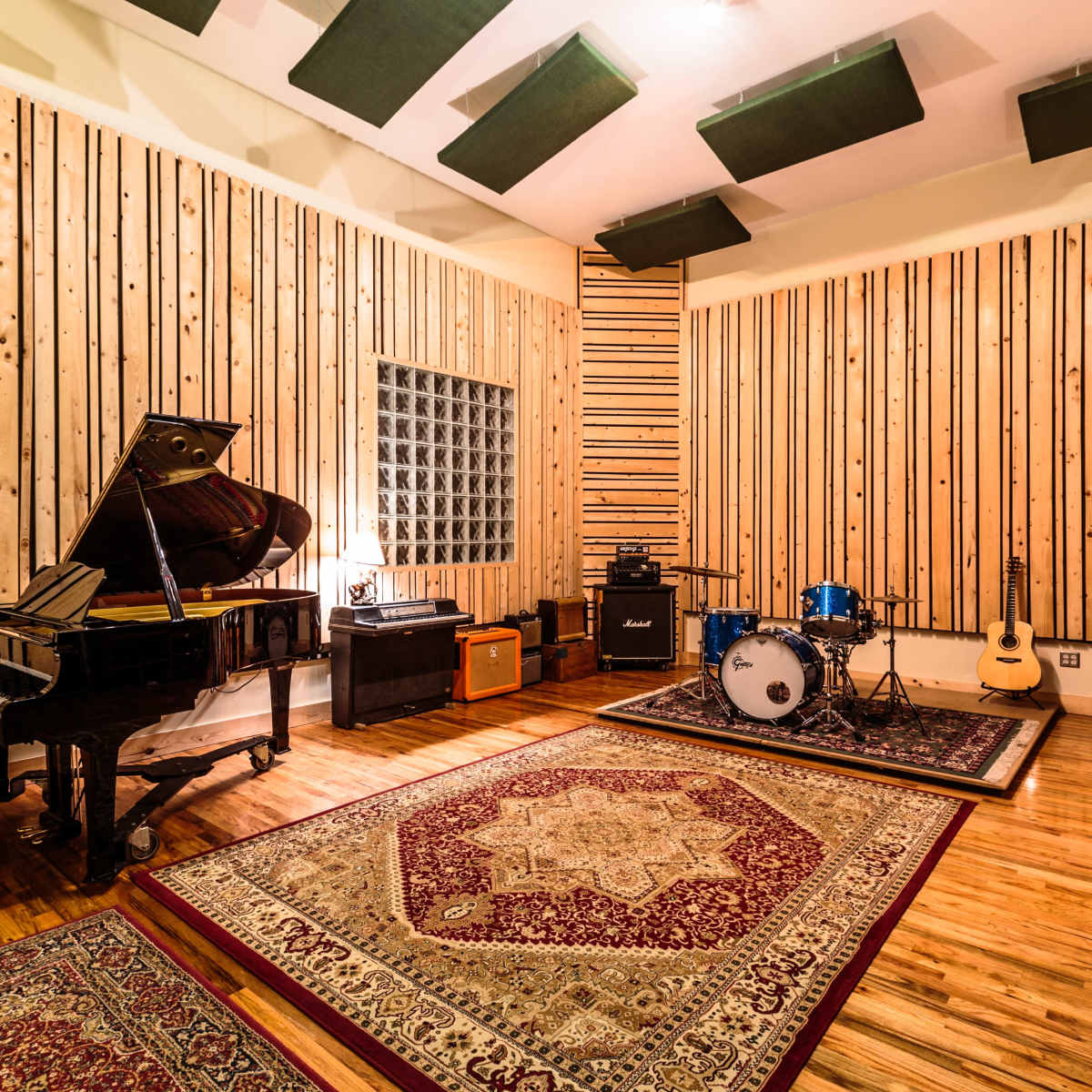 A recording studio with a grand piano, a drum set, amplifiers, and soundproof wooden walls.
