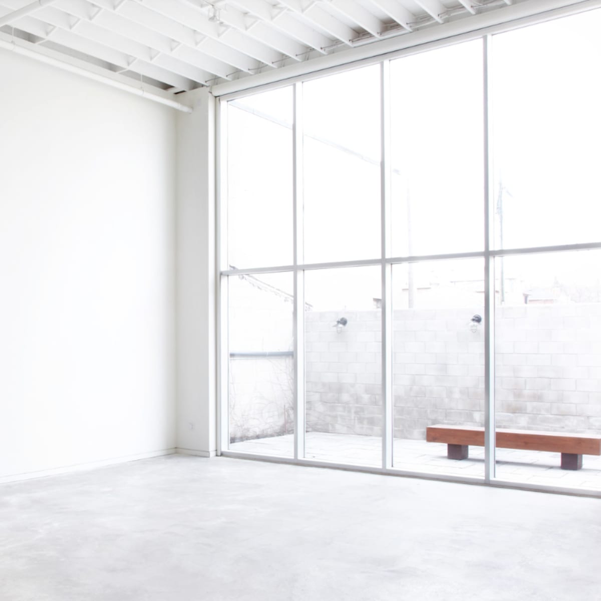 A spacious, bright room with a large window overlooking a small outdoor area and a minimalistic wooden bench.