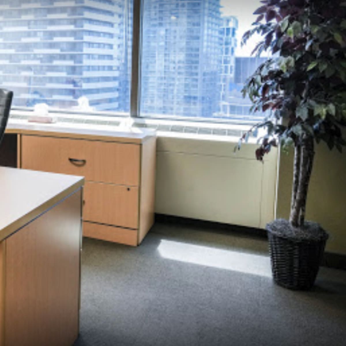 A modern office space with a large desk, a black office chair, and a window overlooking a cityscape.