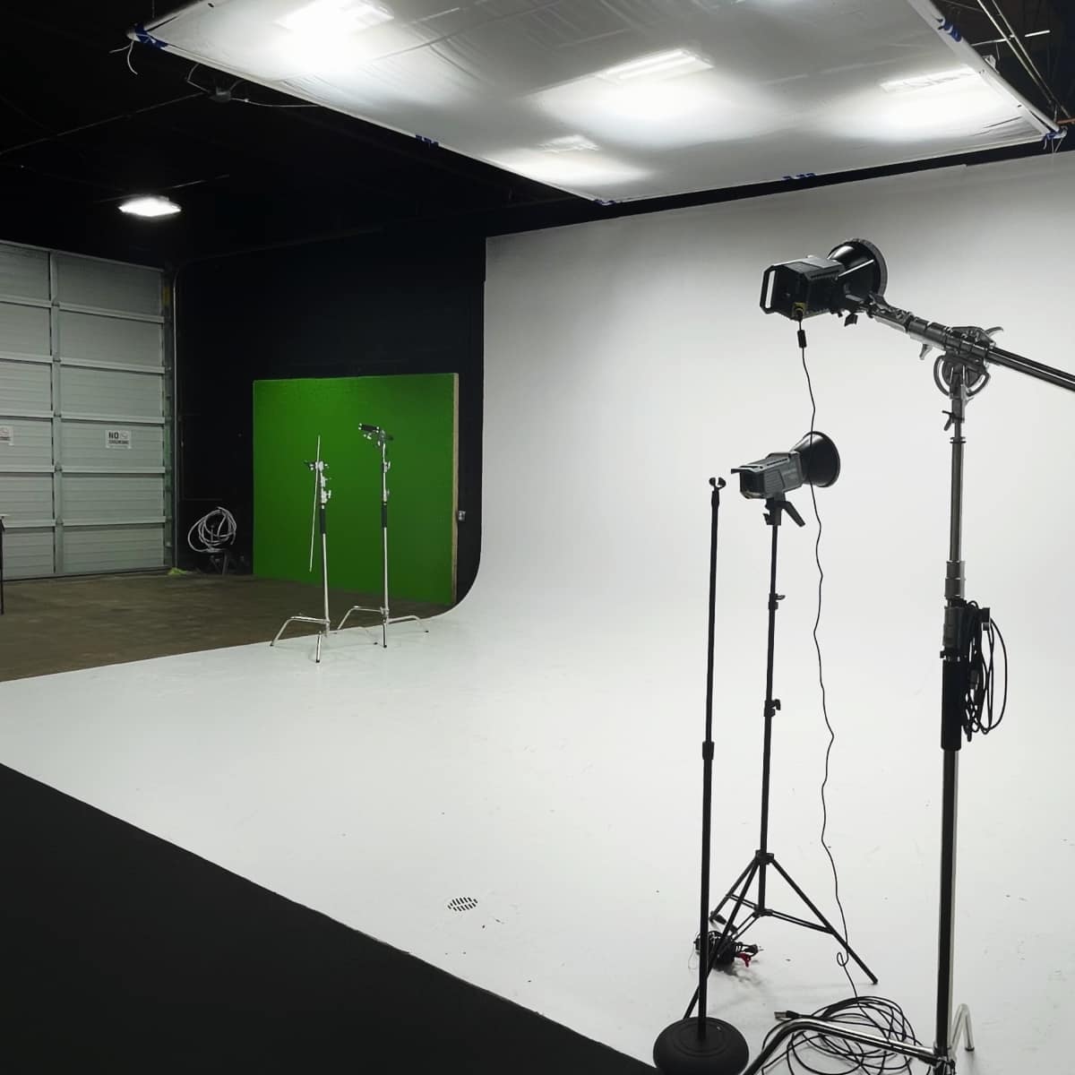A photography studio featuring a white backdrop, a green screen, and several lighting setups on stands.