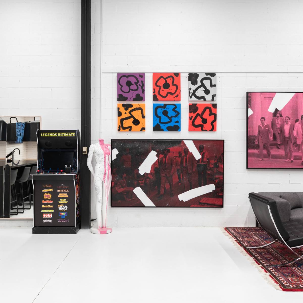 A modern workspace featuring a large wall adorned with colorful artwork, a black display unit, a television, and contemporary furniture arranged in an open layout.