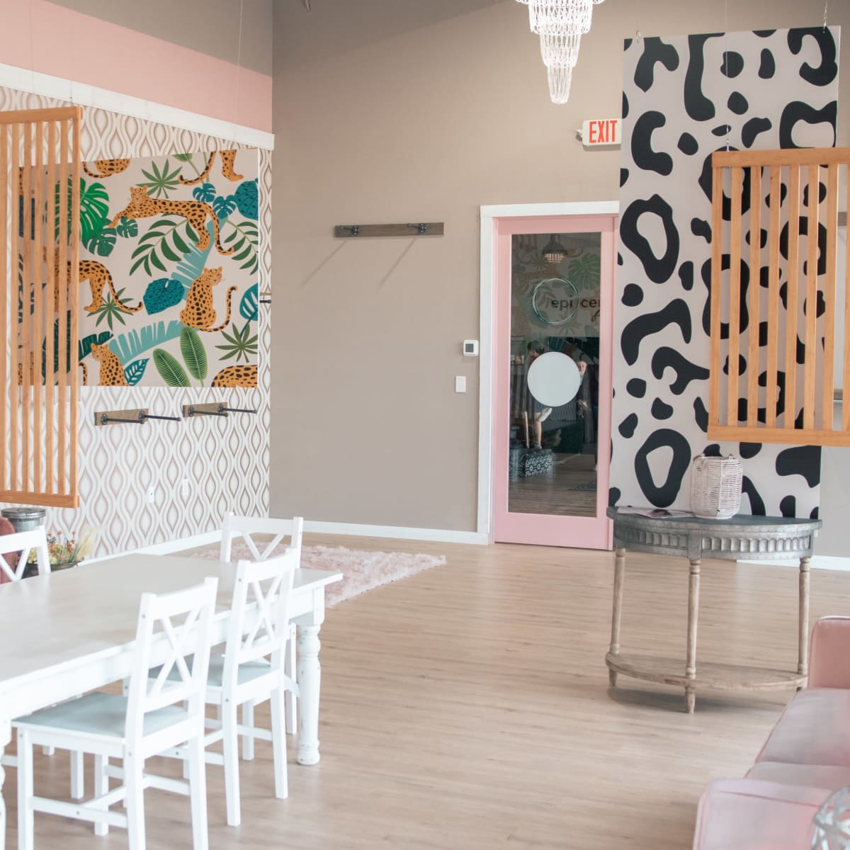 A brightly decorated room with a white dining table surrounded by chairs, colorful wall art featuring plants and animals, and a pink accent wall.