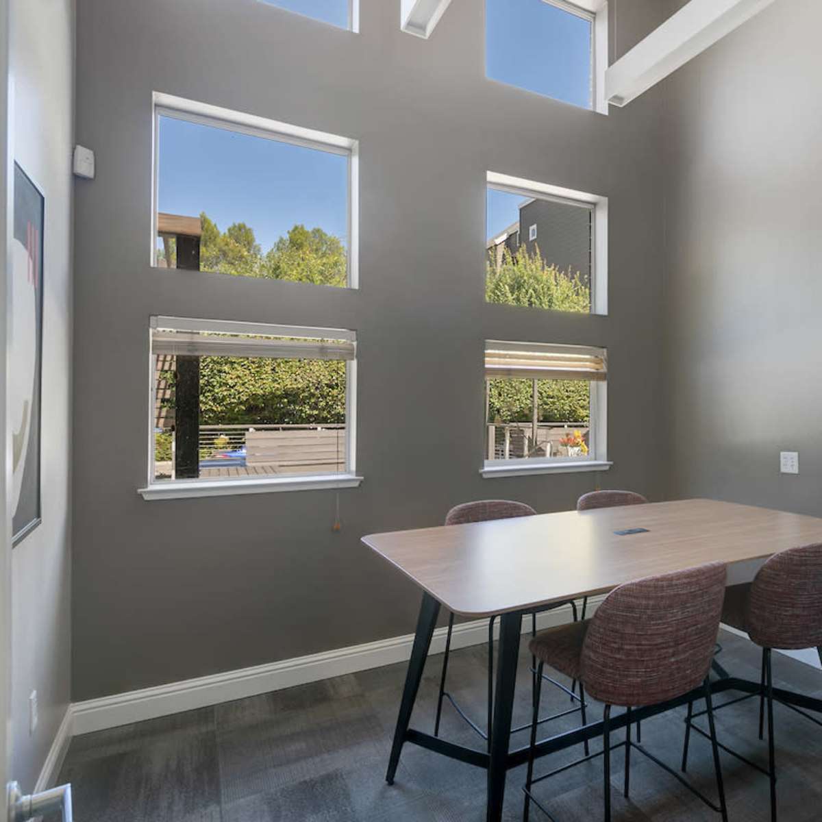 A dining area features a wooden table surrounded by chairs, illuminated by natural light streaming through multiple windows.