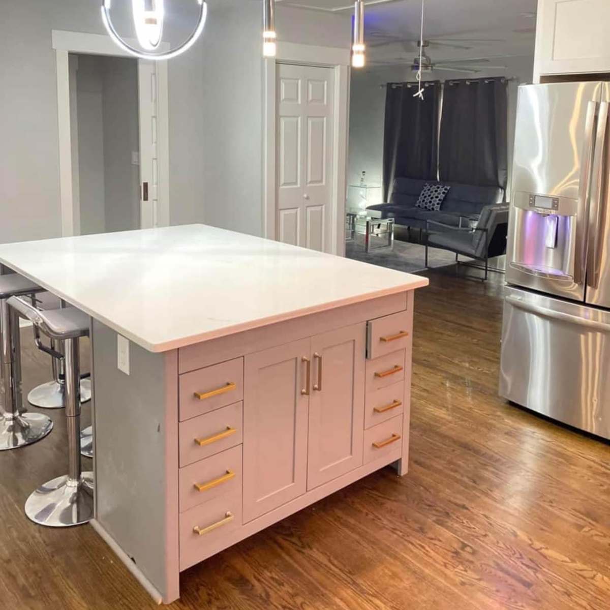 A modern kitchen features a central island with a white countertop, stainless steel appliances, and sleek pendant lighting.