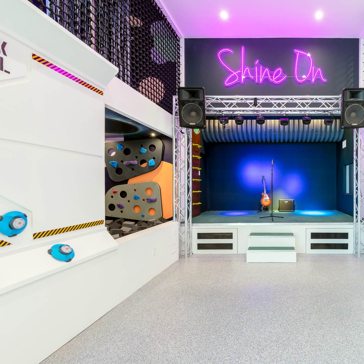 A stage with a guitar and amplifier under a "Shine On" neon sign, accompanied by a climbing wall and a ramp on either side.